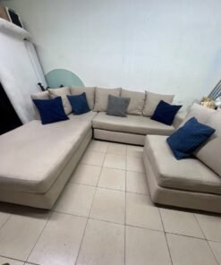 A modern L-shaped corner sofa upholstered in beige fabric, paired with a distinctive standalone lounge chair and accented with contrasting throw pillows in dark blue and patterned gray. - Image 5