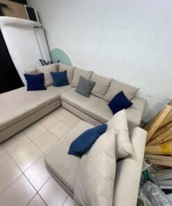 A modern L-shaped corner sofa upholstered in beige fabric, paired with a distinctive standalone lounge chair and accented with contrasting throw pillows in dark blue and patterned gray. - Image 7