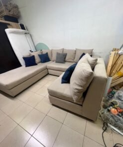 A modern L-shaped corner sofa upholstered in beige fabric, paired with a distinctive standalone lounge chair and accented with contrasting throw pillows in dark blue and patterned gray. - Image 8