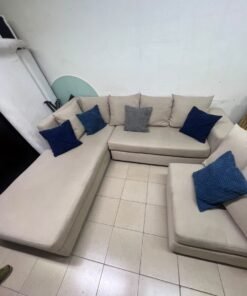 A modern L-shaped corner sofa upholstered in beige fabric, paired with a distinctive standalone lounge chair and accented with contrasting throw pillows in dark blue and patterned gray. - Image 10