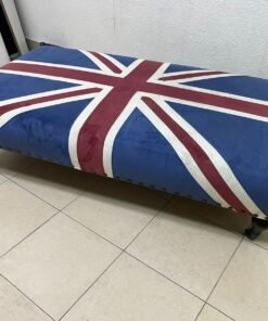 An Ottoman upholstered in luxurious velvet, featuring a vintage British flag design and metal stud detailing along the sides.