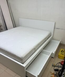 The bed is the high-frame MALM model from IKEA, featuring a white finish and practical under-bed drawers for storing bedding and clothing.