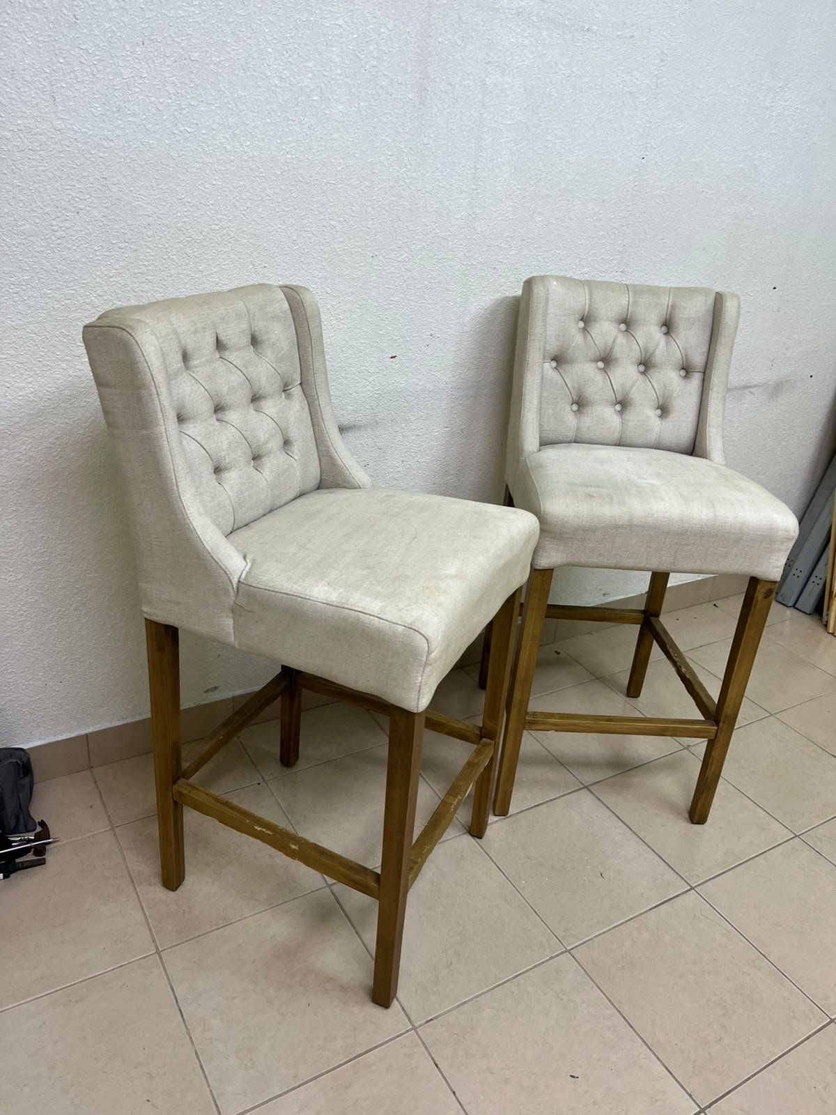 A pair of bar stools featuring a wingback design, beige fabric upholstery with button tufting, and wooden legs. - Image 2