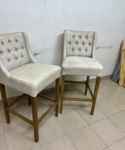 A pair of bar stools featuring a wingback design, beige fabric upholstery with button tufting, and wooden legs. - Image 4