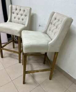 A pair of bar stools featuring a wingback design, beige fabric upholstery with button tufting, and wooden legs. - Image 6