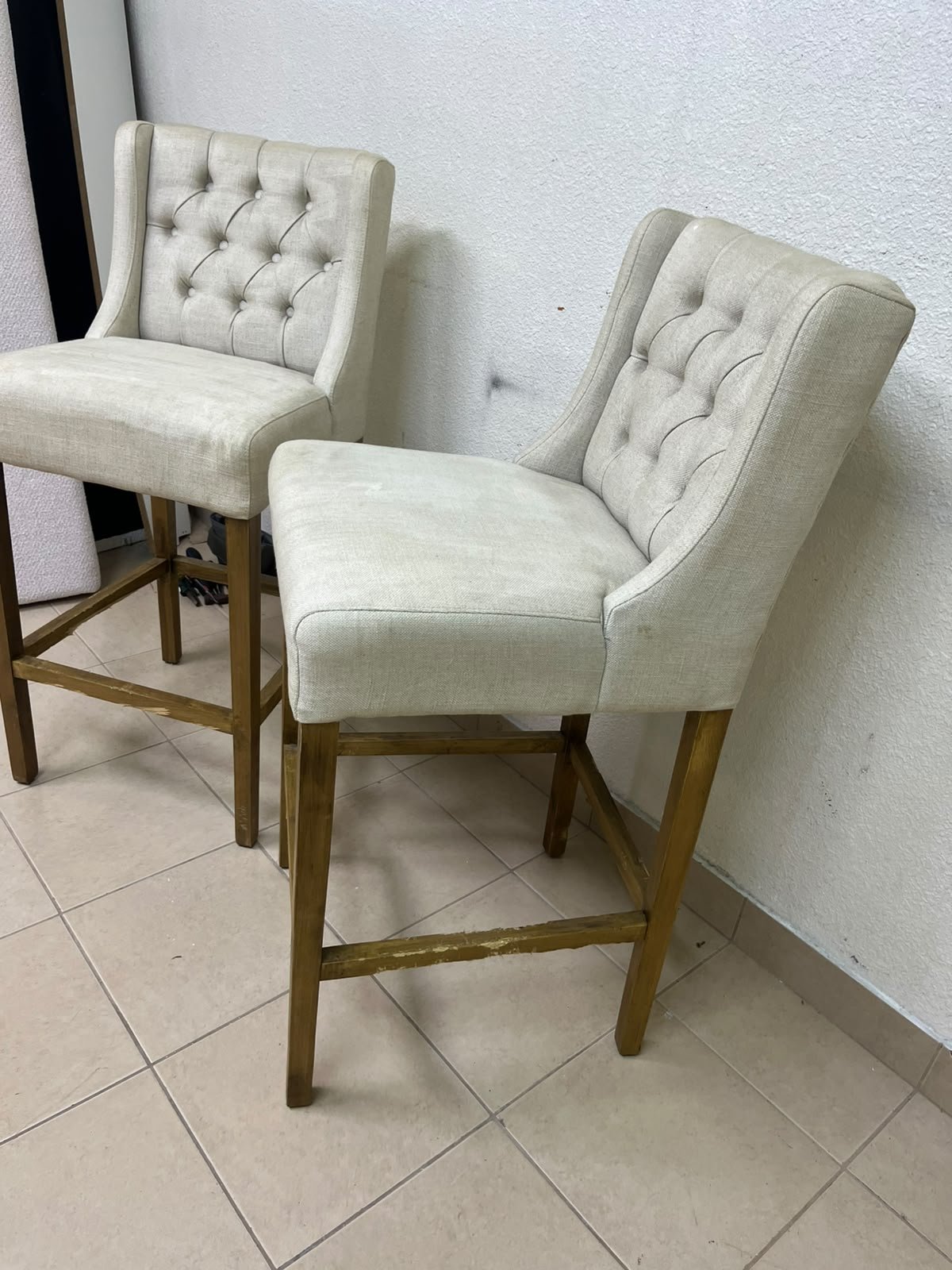 A pair of bar stools featuring a wingback design, beige fabric upholstery with button tufting, and wooden legs. - Image 6