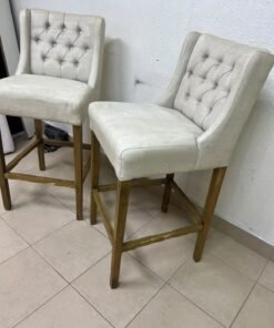 A pair of bar stools featuring a wingback design, beige fabric upholstery with button tufting, and wooden legs. - Image 7