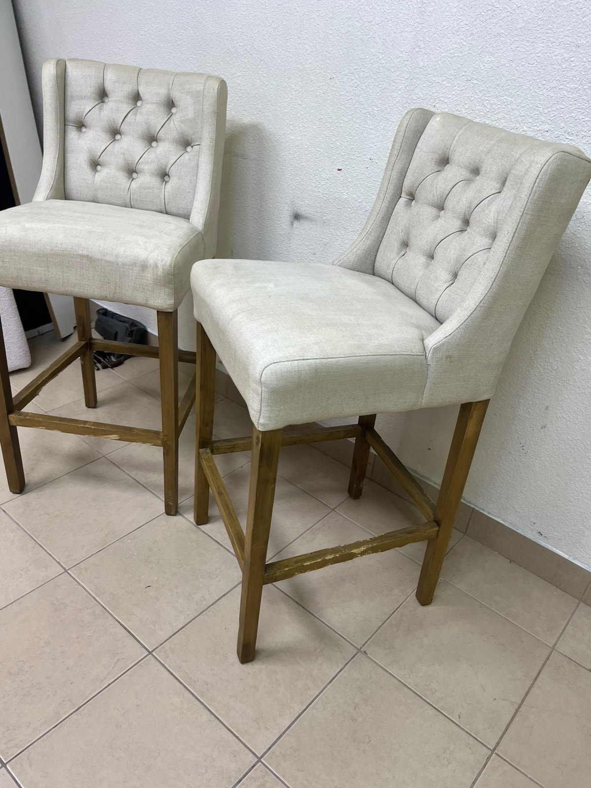 A pair of bar stools featuring a wingback design, beige fabric upholstery with button tufting, and wooden legs. - Image 7