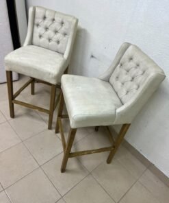A pair of bar stools featuring a wingback design, beige fabric upholstery with button tufting, and wooden legs. - Image 9