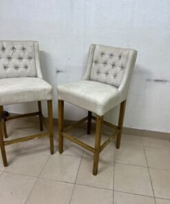 A pair of bar stools featuring a wingback design, beige fabric upholstery with button tufting, and wooden legs. - Image 8