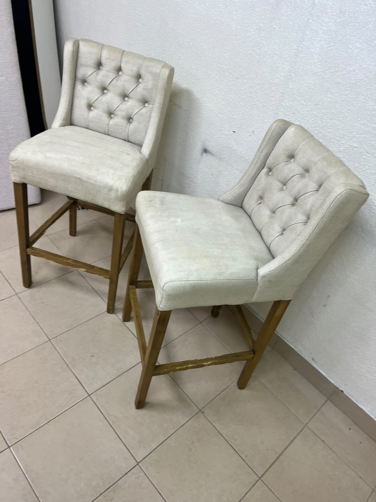 A pair of bar stools featuring a wingback design, beige fabric upholstery with button tufting, and wooden legs. - Image 9