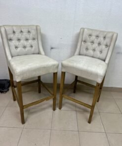 A pair of bar stools featuring a wingback design, beige fabric upholstery with button tufting, and wooden legs. - Image 3