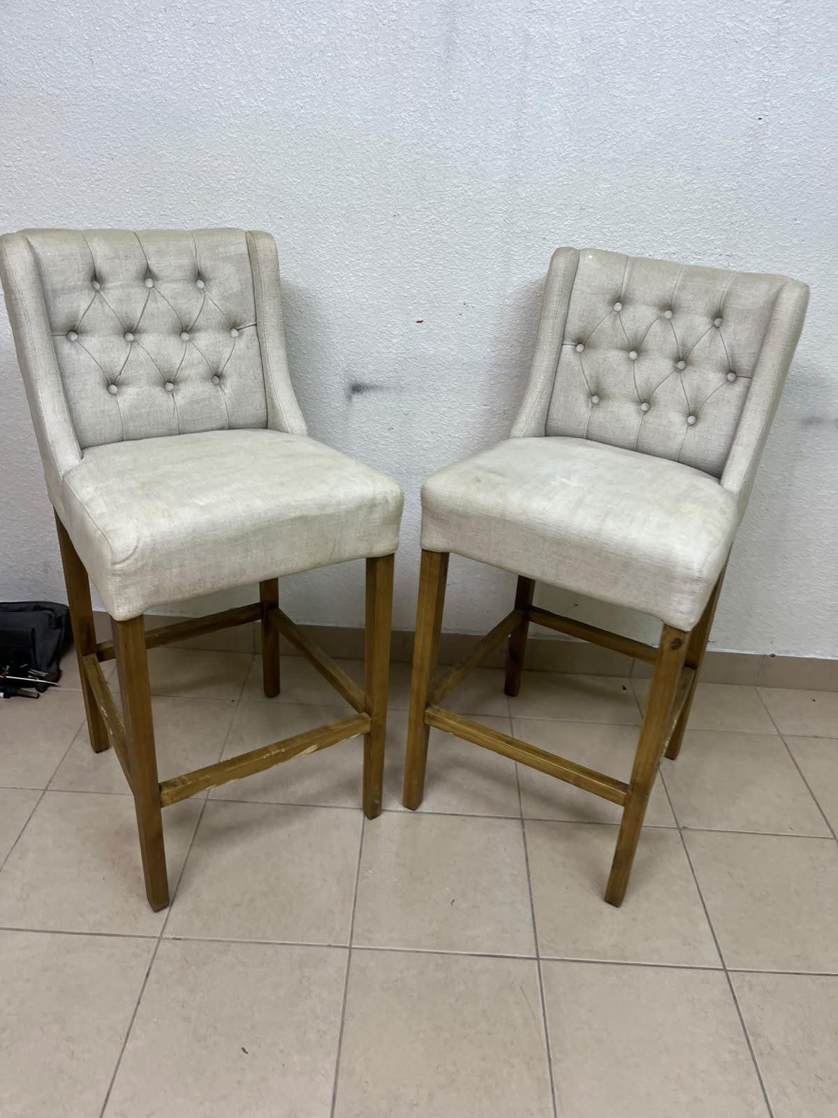 A pair of bar stools featuring a wingback design, beige fabric upholstery with button tufting, and wooden legs. - Image 3
