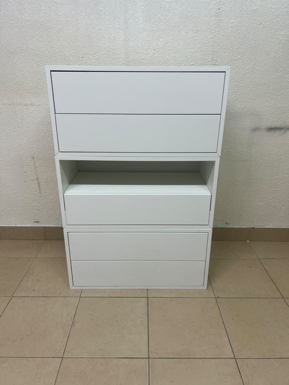 A white storage unit from IKEA’s EKET system, featuring a modular design that combines drawers with open storage space.