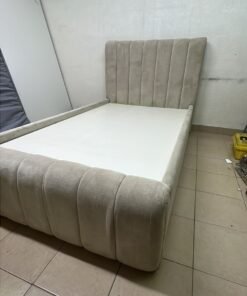 An elegantly designed, modern upholstered bed featuring a high headboard padded with prominent vertical lines and a curved footboard.