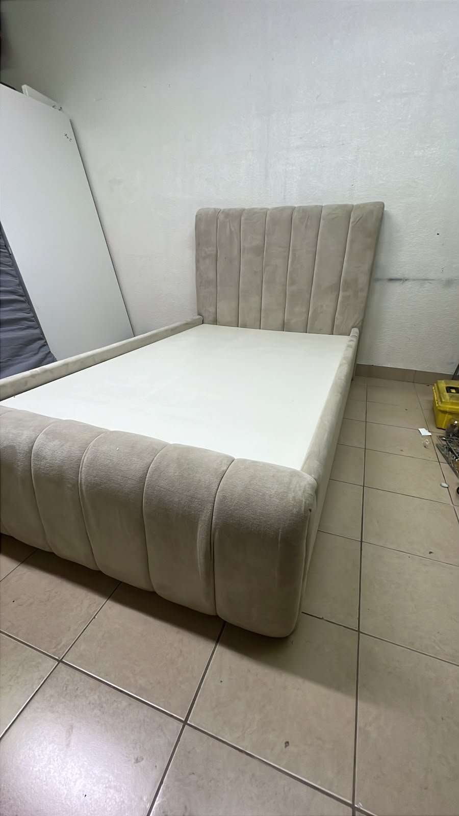 An elegantly designed, modern upholstered bed featuring a high headboard padded with prominent vertical lines and a curved footboard.