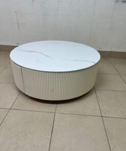 This round coffee table is elegant, featuring a cream-colored ribbed base and a stone tabletop with a marble-like pattern.