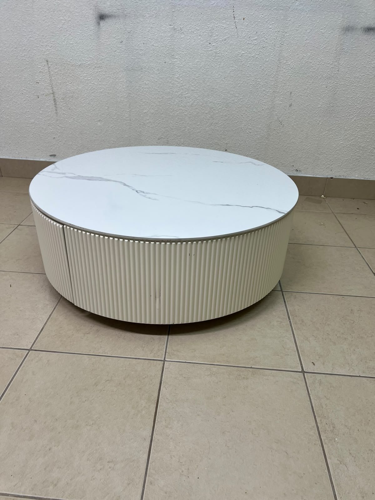 This round coffee table is elegant, featuring a cream-colored ribbed base and a stone tabletop with a marble-like pattern.