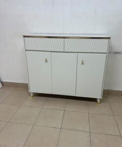 A white shoe cabinet or entryway storage unit (console) featuring a modern design, ribbed upper drawers, and gold accents on the handles and legs.