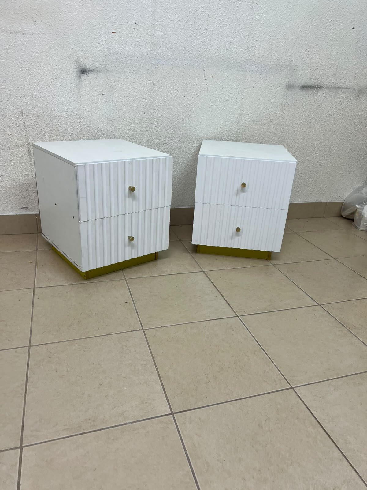Modern white bedside tables featuring an elegant vertical ribbed design, with attractive gold accents on the handles and base.