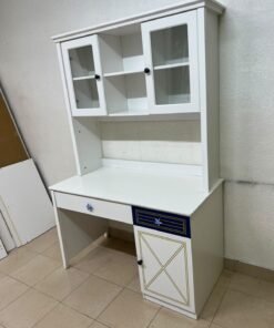 A white study desk featuring an overhead storage unit (a hutch or bookcase with glass-fronted cabinets), shelves, and a spacious work surface, along with a drawer and a lower cabinet accented with blue and gold star motifs and geometric patterns; a practical design suitable for children's or students' rooms for organizing books and school supplies.