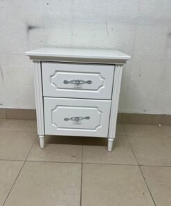 The elegant white side table with two drawers is distinguished by its decorative details and prominent silver handles.