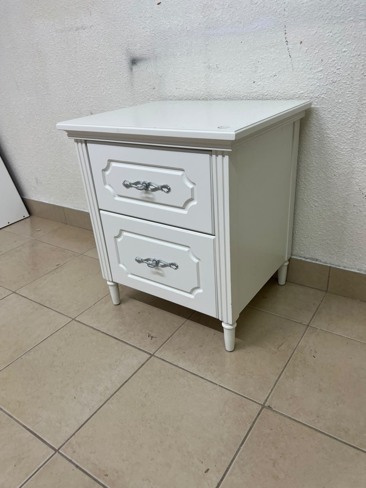 The elegant white side table with two drawers is distinguished by its decorative details and prominent silver handles. - Image 3