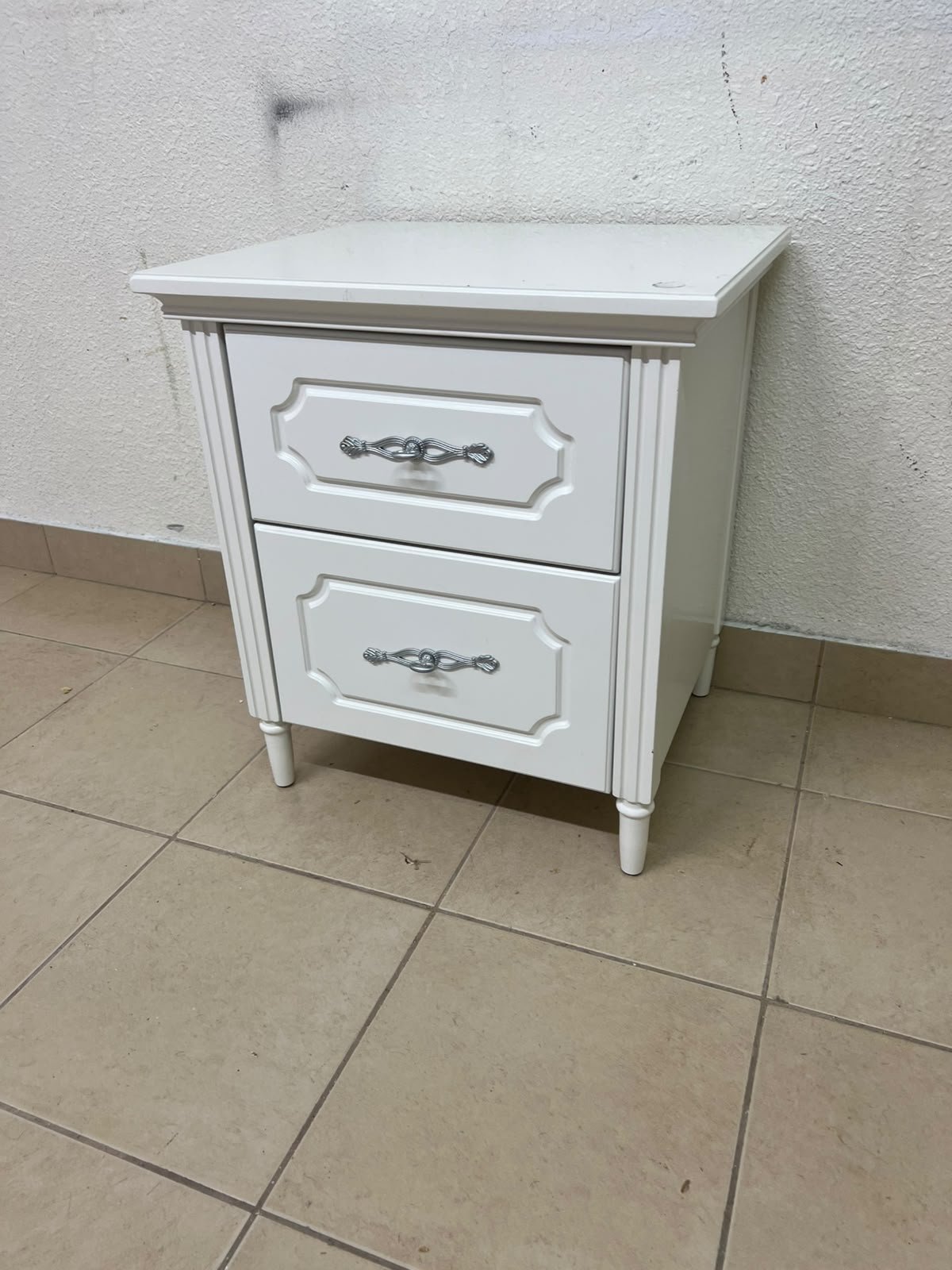 The elegant white side table with two drawers is distinguished by its decorative details and prominent silver handles. - Image 4