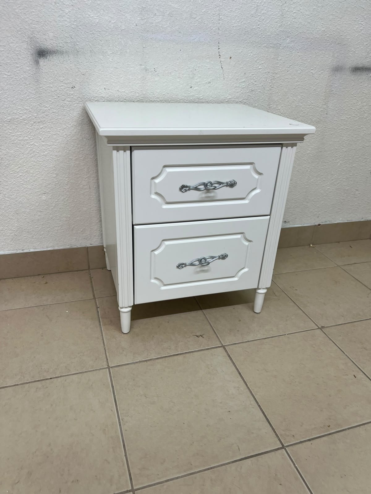 The elegant white side table with two drawers is distinguished by its decorative details and prominent silver handles. - Image 6
