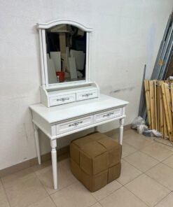 A white vanity table featuring a mirror and both upper and lower drawers, accompanied by a square brown stool upholstered in mesh fabric.
