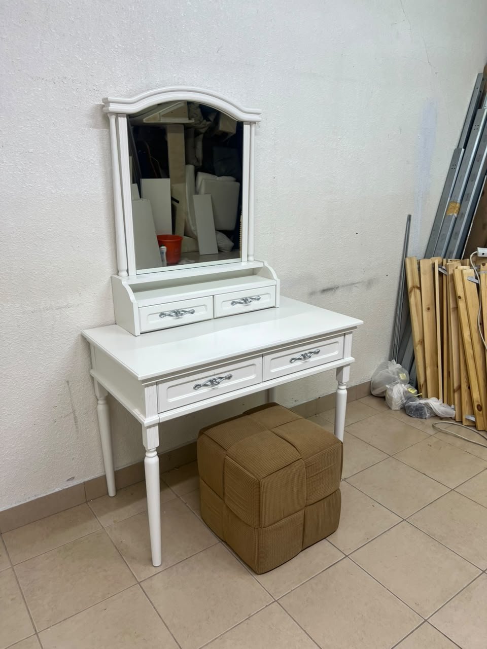 A white vanity table featuring a mirror and both upper and lower drawers, accompanied by a square brown stool upholstered in mesh fabric.