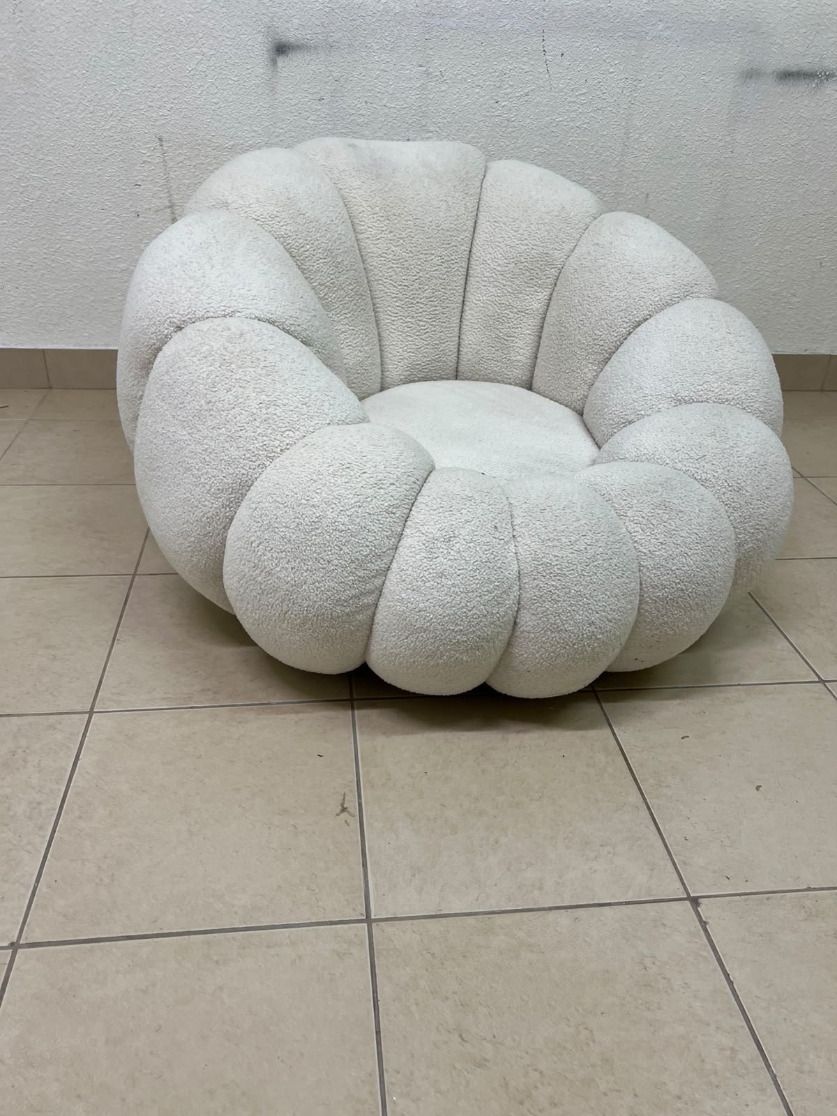 The Fana "Flower" chair from Home Centre is a lounge chair featuring a floral-inspired design and upholstered in soft, comfortable bouclé fabric; it is distinguished by its rounded shape—resembling petals or a pumpkin.