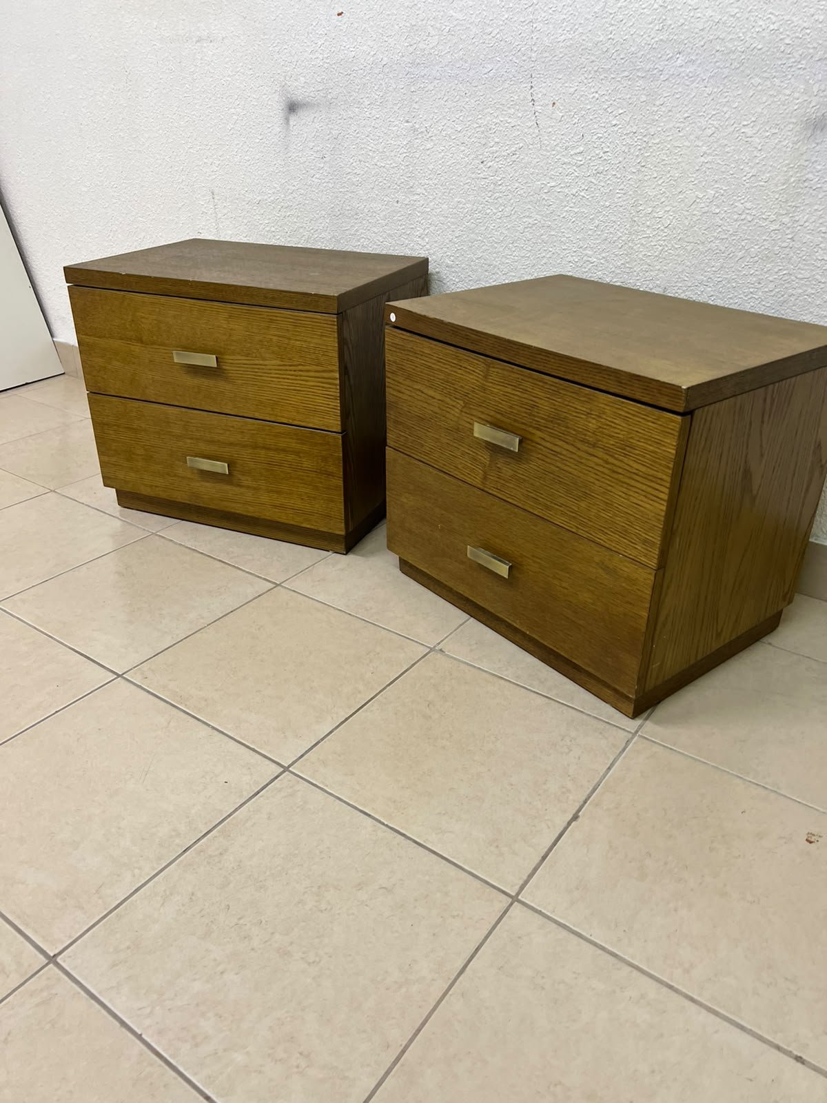 Two wooden side tables in a warm brown hue, featuring an elegant design with two drawers and distinctive metal handles.