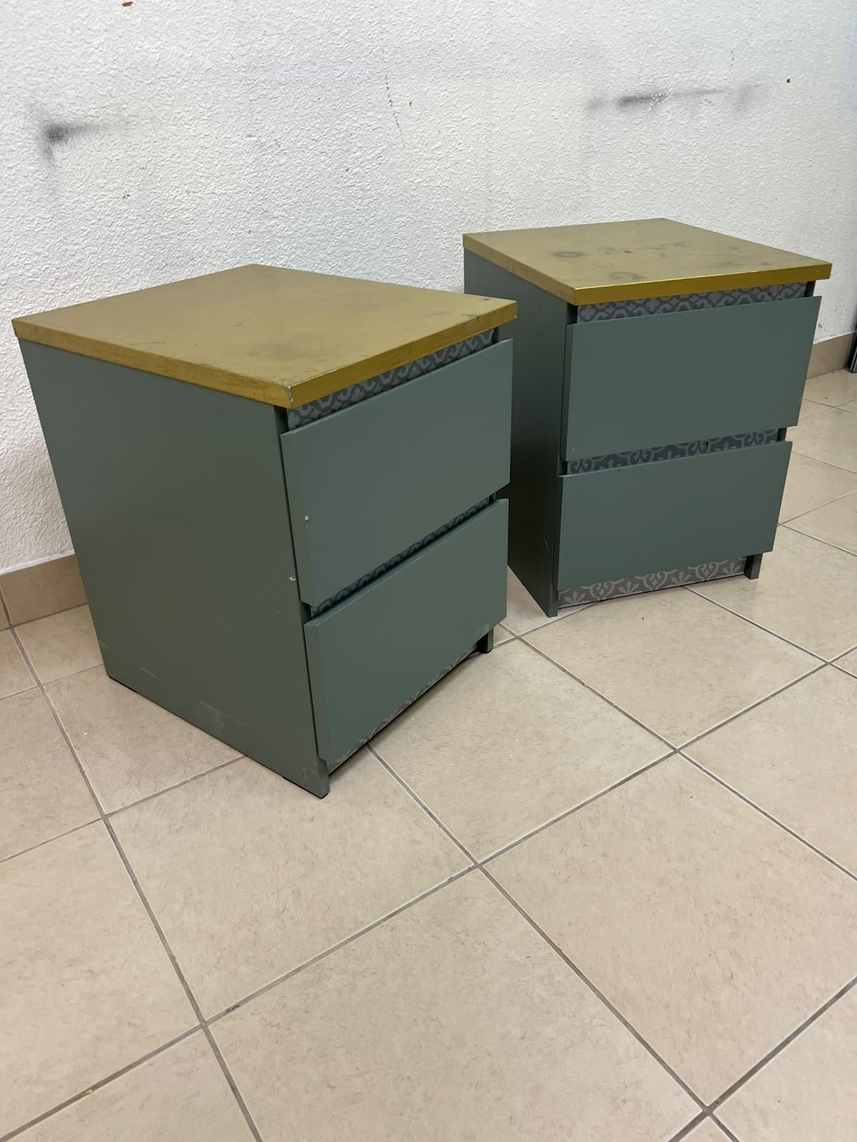 A bedside table featuring a minimalist design, grey-green drawers, and a wooden or yellowish top surface; the style resembles modern storage furniture.