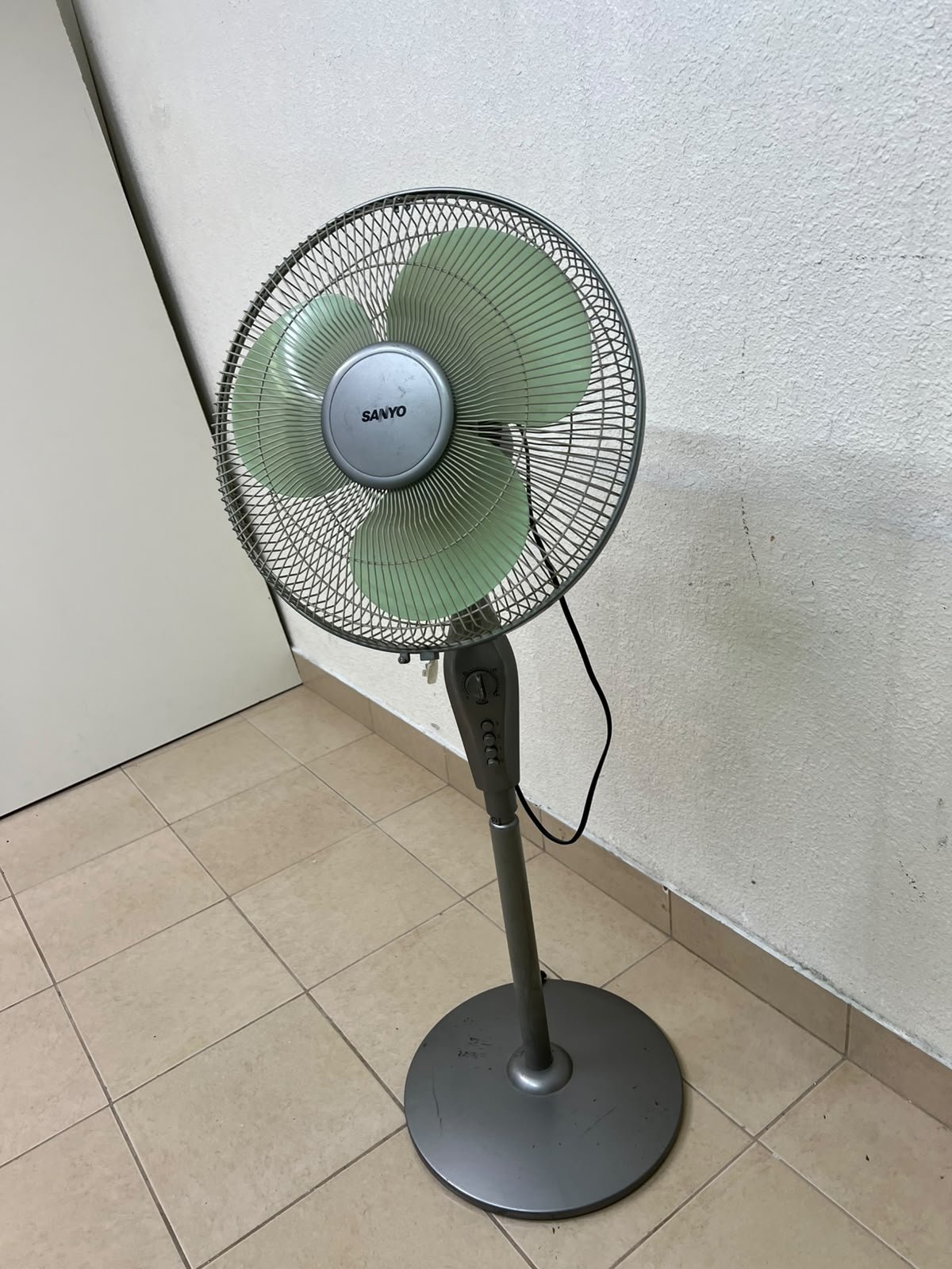 A Sanyo-branded grey pedestal fan featuring light green blades and a circular base.