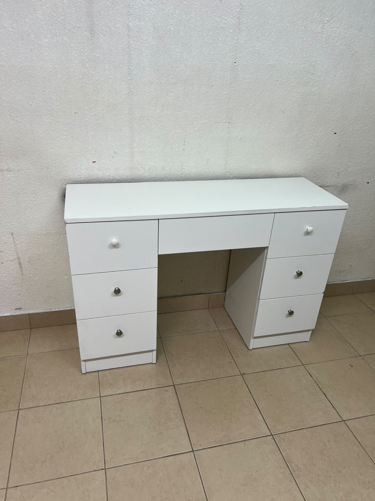 A white vanity desk featuring a modern, practical design, complete with seven storage drawers and elegant round handles.