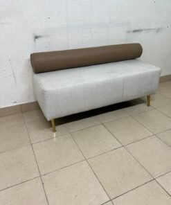 The light-gray upholstered seat, featuring a brown cylindrical backrest and gold legs, is a stylish, modern piece of furniture that adds a distinctive touch to the décor.