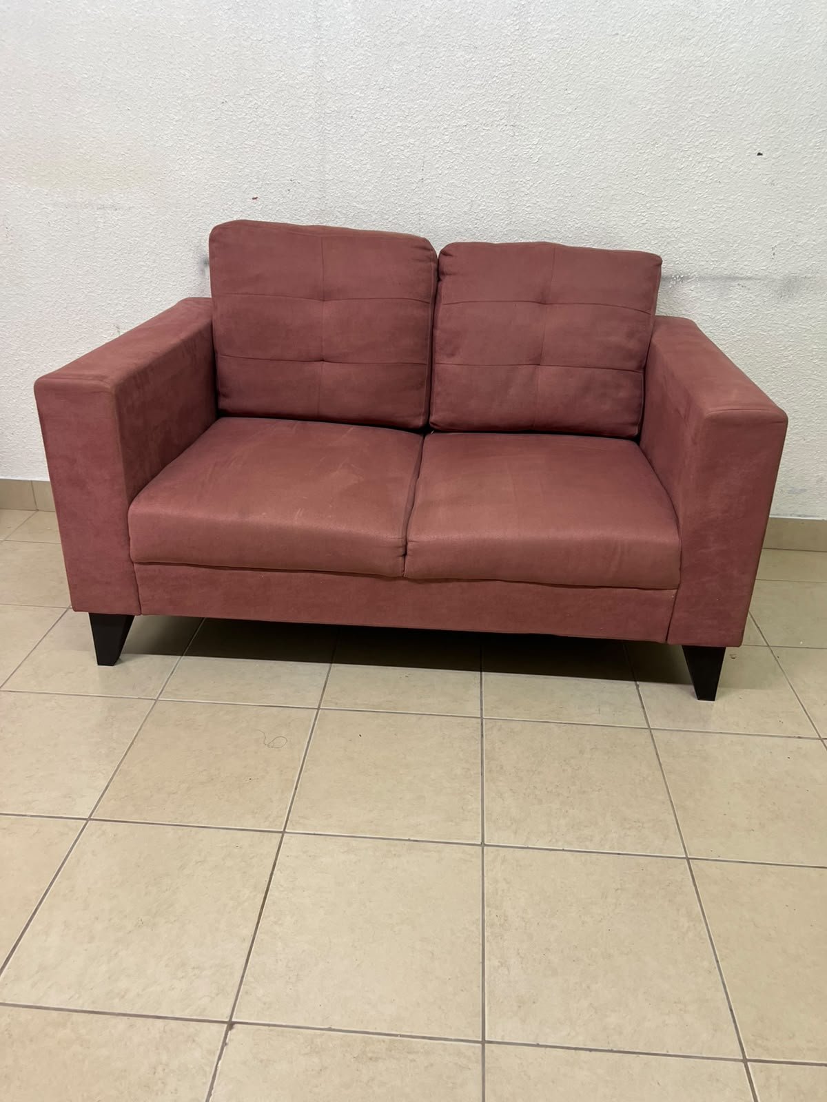 A red or dark pink two-seater fabric sofa featuring wide armrests and back cushions adorned with a checkered pattern.