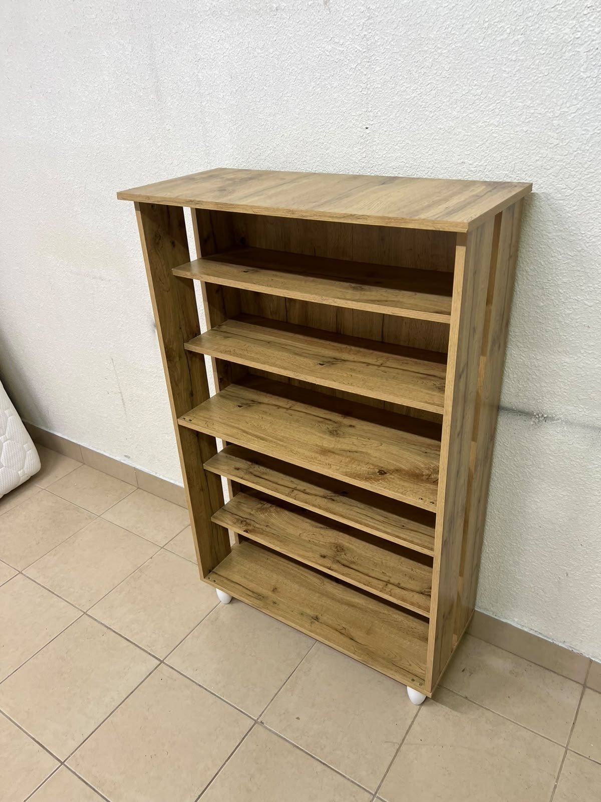 The wooden shoe cabinet, featuring open shelves and small white legs, is a practical and stylish piece for organizing the entryway.