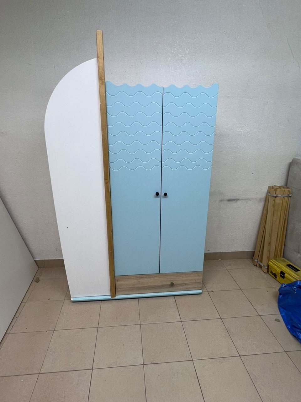 The photo shows a children's wardrobe with a distinctive nautical design in blue and white with wooden details and wave-like top edges.