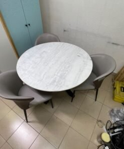 An elegant 110 cm round dining table featuring a white marble top and a black crossed metal base, surrounded by curved grey chairs with an ergonomic design. - Image 3