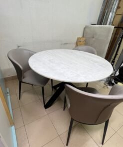 An elegant 110 cm round dining table featuring a white marble top and a black crossed metal base, surrounded by curved grey chairs with an ergonomic design.