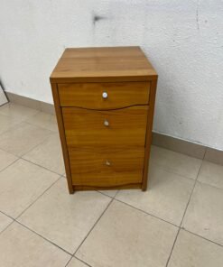 A wooden side table (nightstand) featuring three drawers with slightly curved fronts and small, round handles.