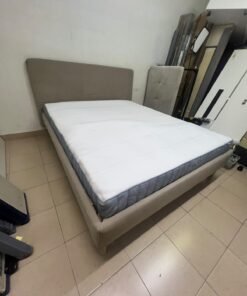 An IKEA bed with a foam and spring mattress—resembling the VALEVÅG or VESTERÖY models—featuring an upholstered bed frame in light gray or beige.