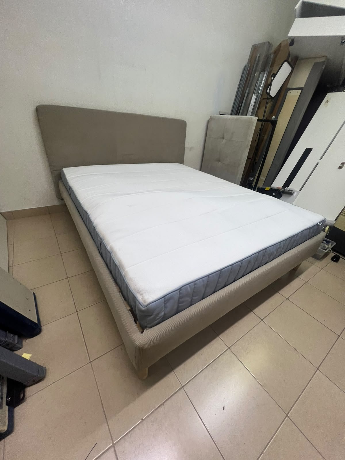 An IKEA bed with a foam and spring mattress—resembling the VALEVÅG or VESTERÖY models—featuring an upholstered bed frame in light gray or beige.
