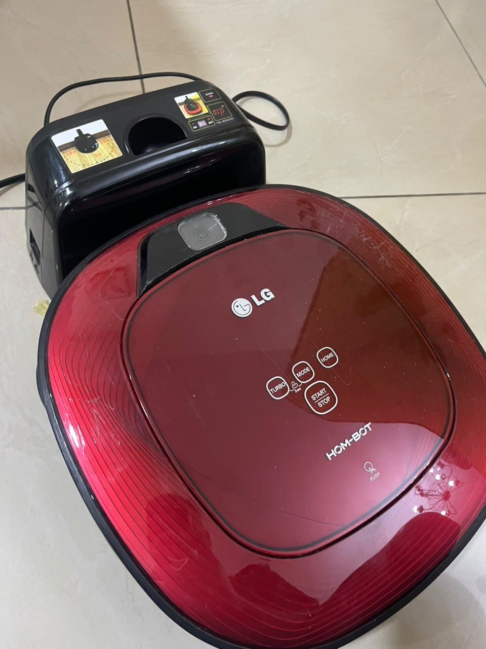 Red square-shaped robotic vacuum cleaner by LG (model LG Hom-Bot VR6270LVMB) with its charging base. - Image 2