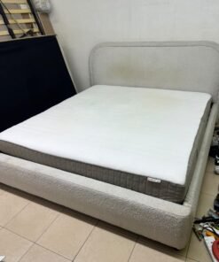 Modern upholstered double bed (featuring curved lines on the headboard and frame, covered in a textured fabric—such as bouclé, borg, or a woven textile—in a light beige or off-white shade), with a white top mattress resting on the bed base. 180x200 cm.