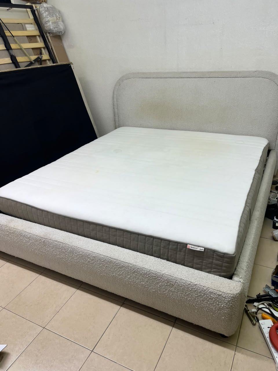 Modern upholstered double bed (featuring curved lines on the headboard and frame, covered in a textured fabric—such as bouclé, borg, or a woven textile—in a light beige or off-white shade), with a white top mattress resting on the bed base. 180x200 cm.