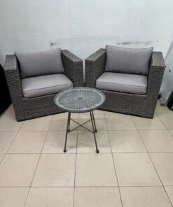 A compact outdoor seating set consisting of two grey synthetic rattan (PE Rattan) armchairs with comfortable grey cushions, plus a round table with a glass top.