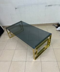 A modern coffee table featuring a dark glass top (tempered or smoked glass) and a shiny gold metal frame and base, distinguished by an interlocking geometric design on the sides. - Image 9